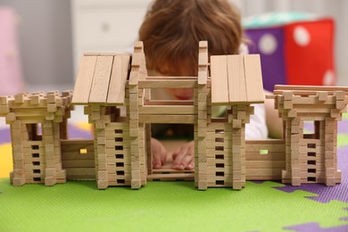 Little boy playing with wooden entry gate on puzzle mat in room, selective focus. Child's toy