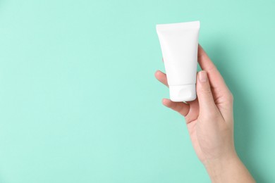 Woman with tube of hand cream on turquoise background, top view. Space for text