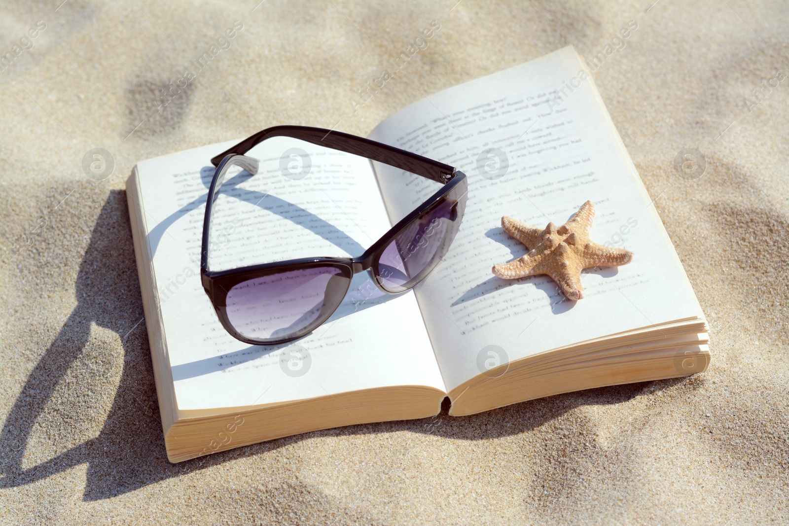 Photo of Beautiful sunglasses, book and starfish on sand