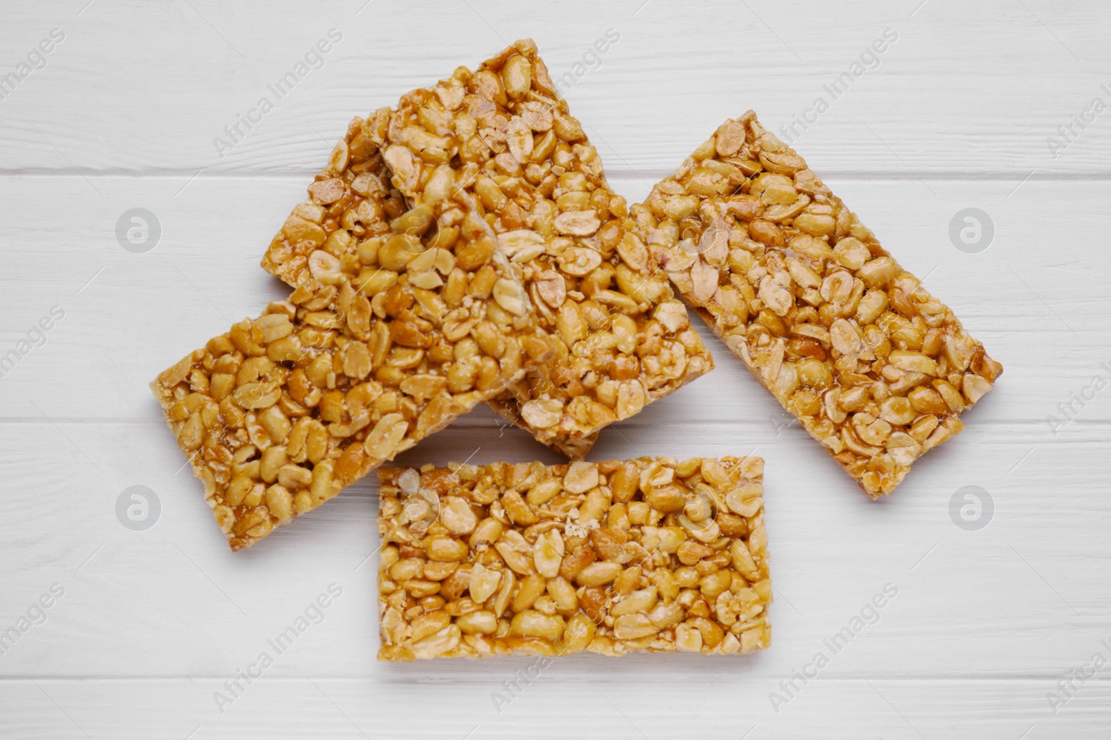 Photo of Tasty peanut bars (kozinaki) on white wooden table, flat lay