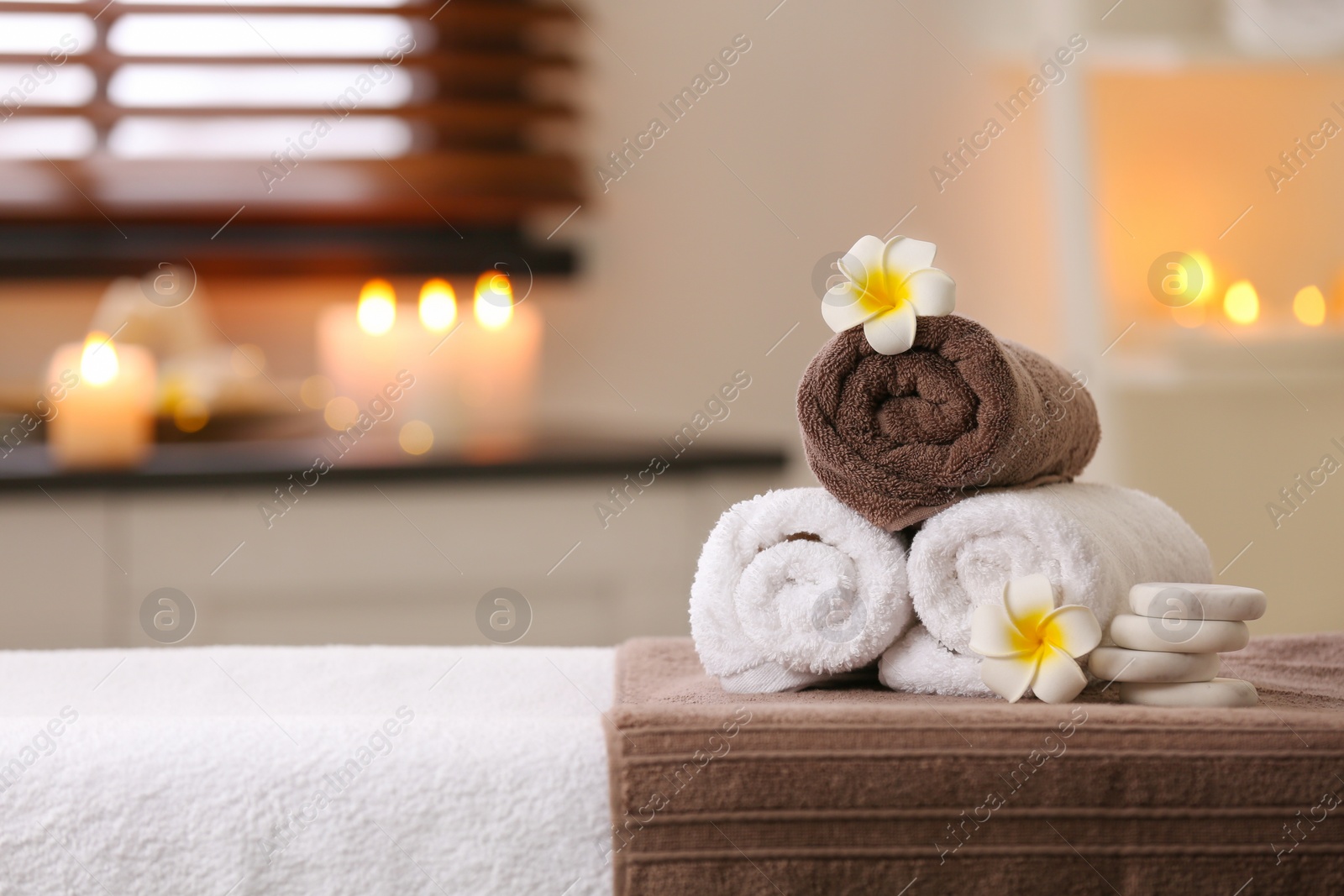 Photo of Composition with towels, flowers and stones on massage table in spa salon. Space for text