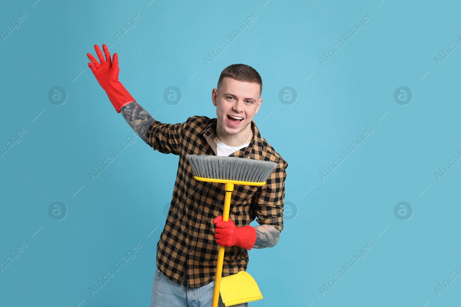 Photo of Handsome young man with floor brush singing on light blue background. Space for text