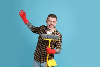 Photo of Handsome young man with floor brush singing on light blue background. Space for text