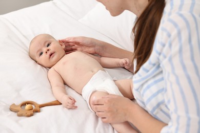 Woman applying body cream onto baby`s skin on bed, closeup