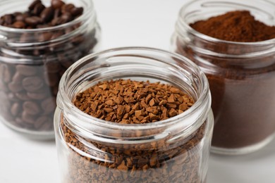 Photo of Jars with instant, ground coffee and roasted beans on white table, closeup