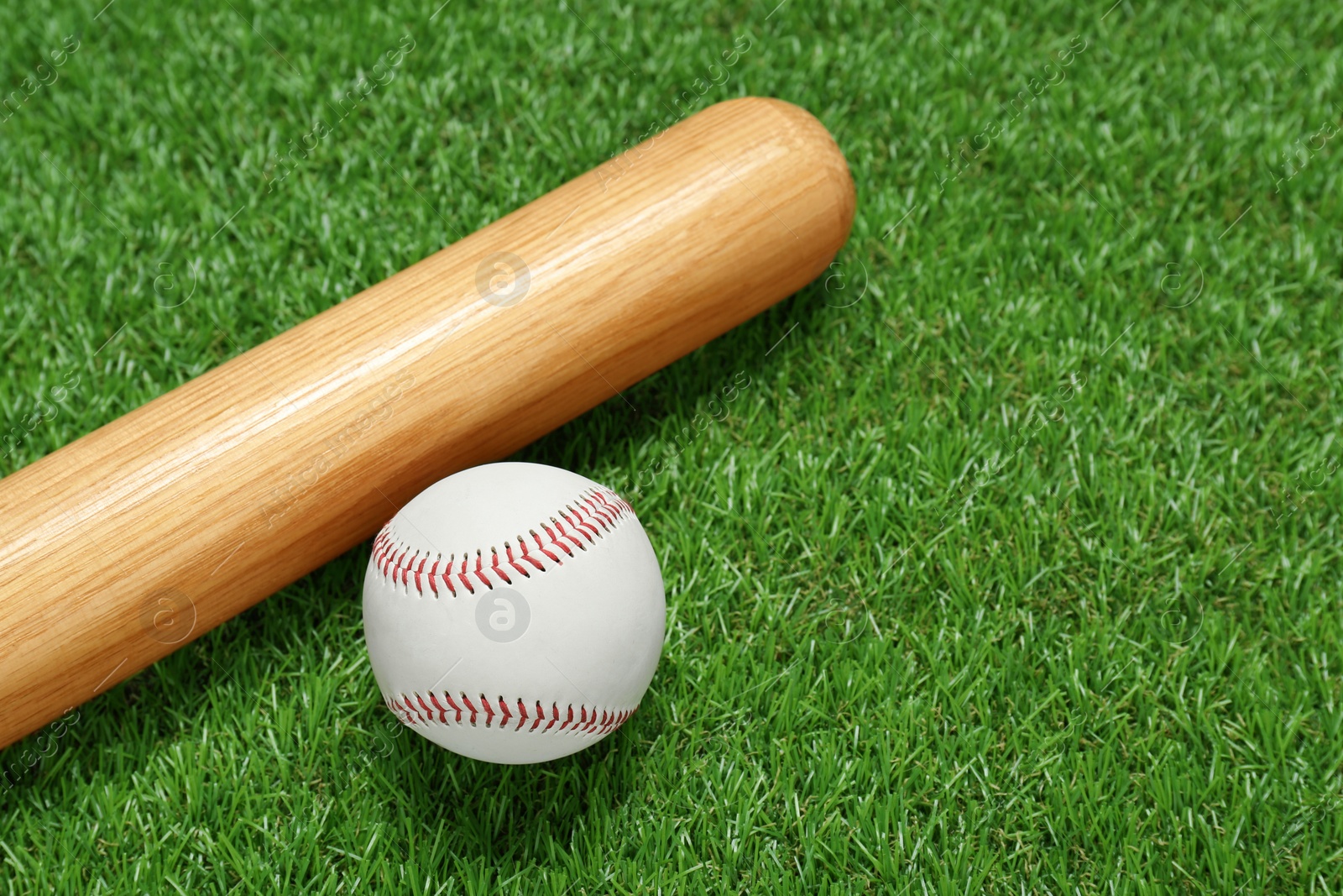 Photo of Wooden baseball bat and ball on green grass, closeup. Sports equipment