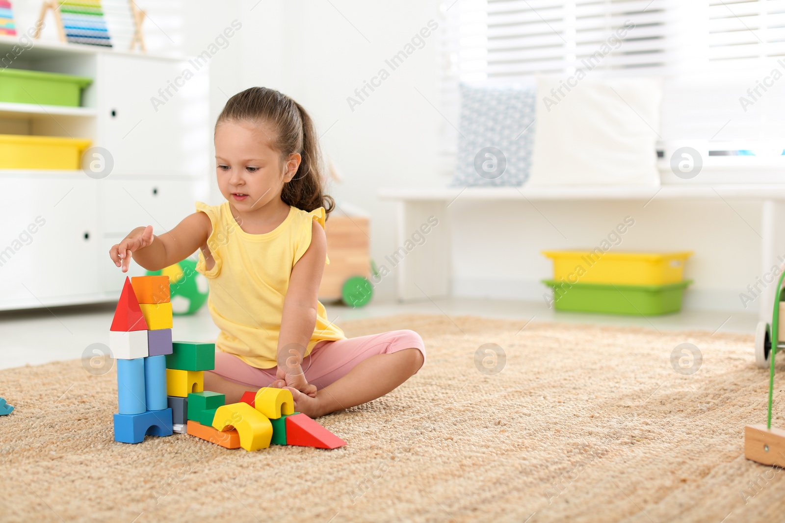 Photo of Cute little girl playing with colorful blocks on floor indoors, space for text. Educational toy