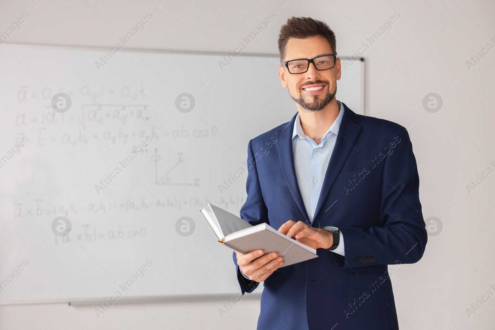 Photo of Happy teacher with book at whiteboard in classroom during math lesson