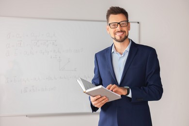 Photo of Happy teacher with book at whiteboard in classroom during math lesson