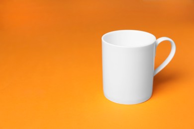 Photo of One white ceramic mug on orange background, space for text