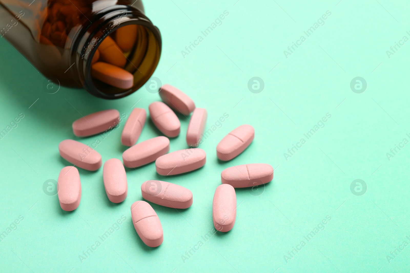 Photo of Vitamin pills and bottle on mint color background, closeup. Space for text