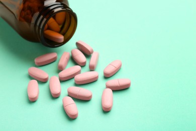 Vitamin pills and bottle on mint color background, closeup. Space for text