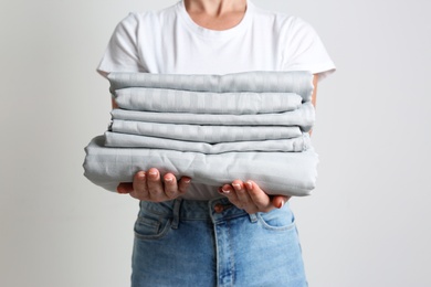 Photo of Woman holding stack of clean bed linens on light grey background