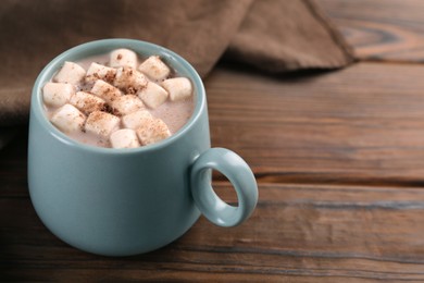 Photo of Cup of aromatic hot chocolate with marshmallows and cocoa powder on wooden table, closeup. Space for text