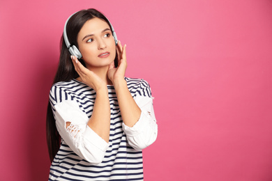 Young woman listening to audiobook on pink background. Space for text