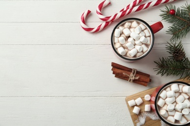 Photo of Hot drinks with marshmallows, candy canes and fir branches on white wooden table, flat lay. Space for text