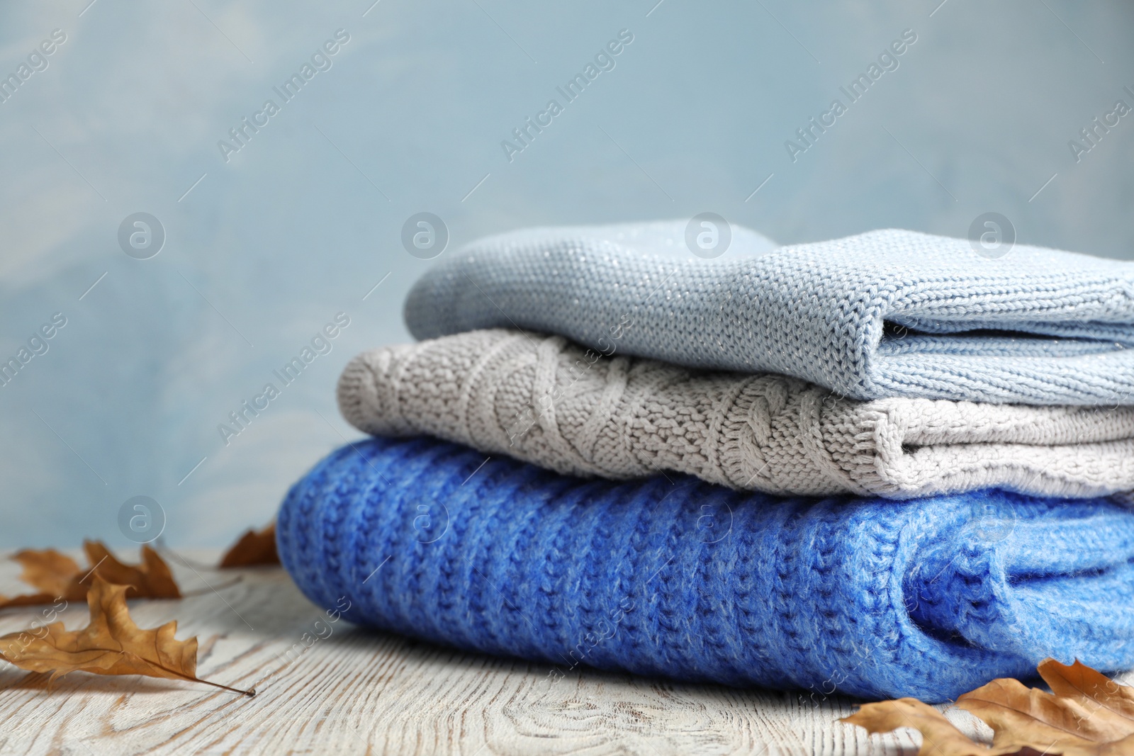 Photo of Stack of folded knitted sweaters and autumn leaves on table