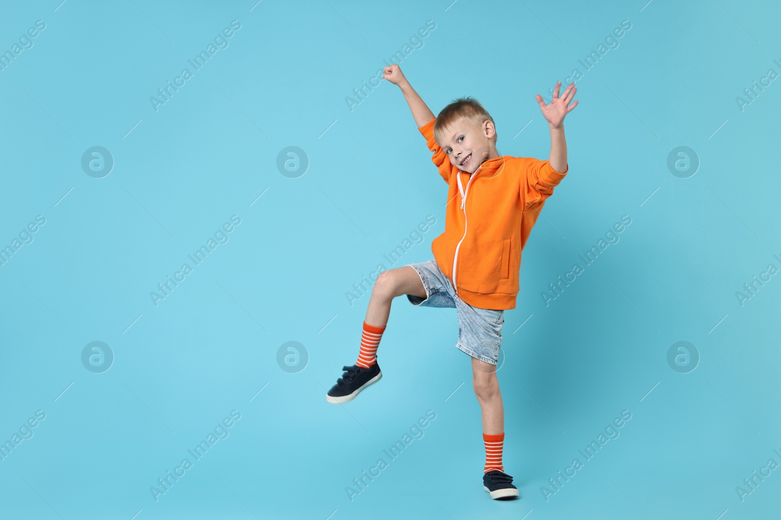 Photo of Happy little boy dancing on light blue background. Space for text