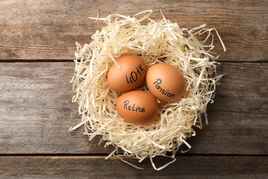 Photo of Eggs with words PENSION, RETIRE and 401k in nest on wooden background, top view