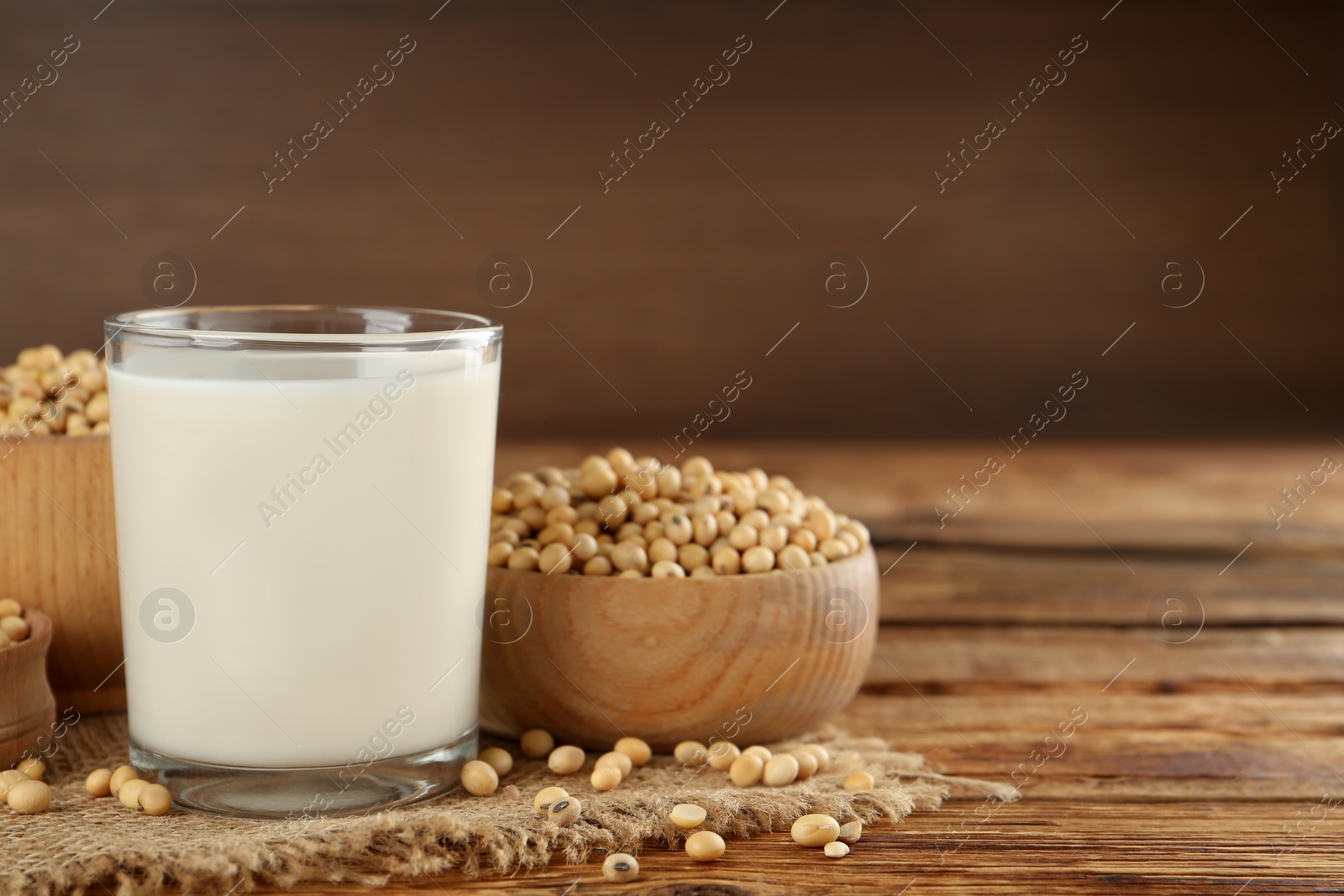 Photo of Glass with fresh soy milk and grains on wooden table. Space for text