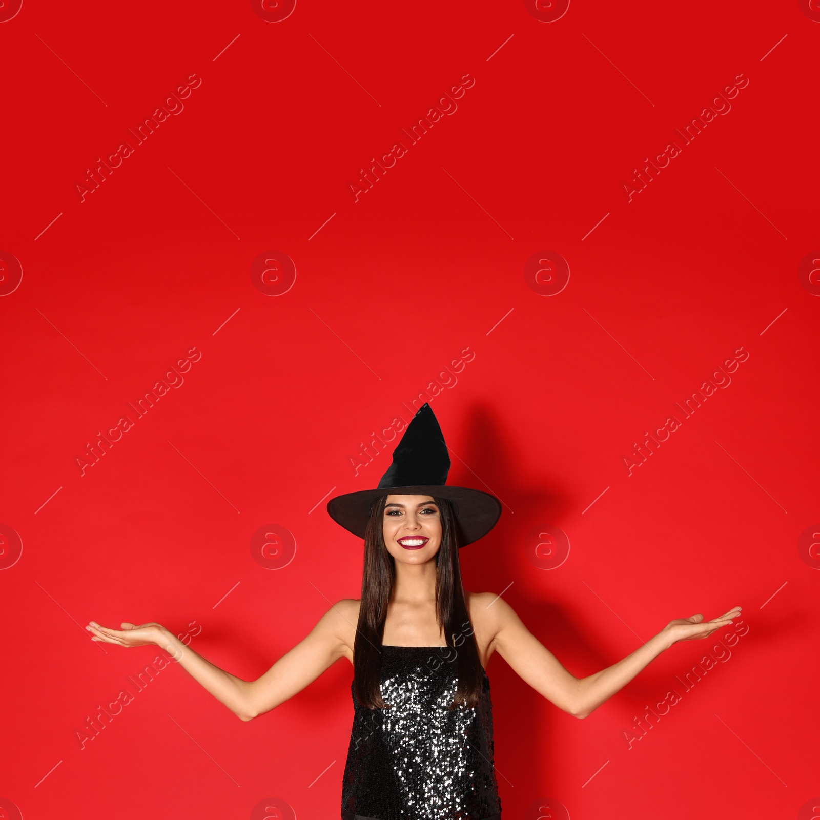 Photo of Beautiful young woman wearing witch costume for Halloween party on red background