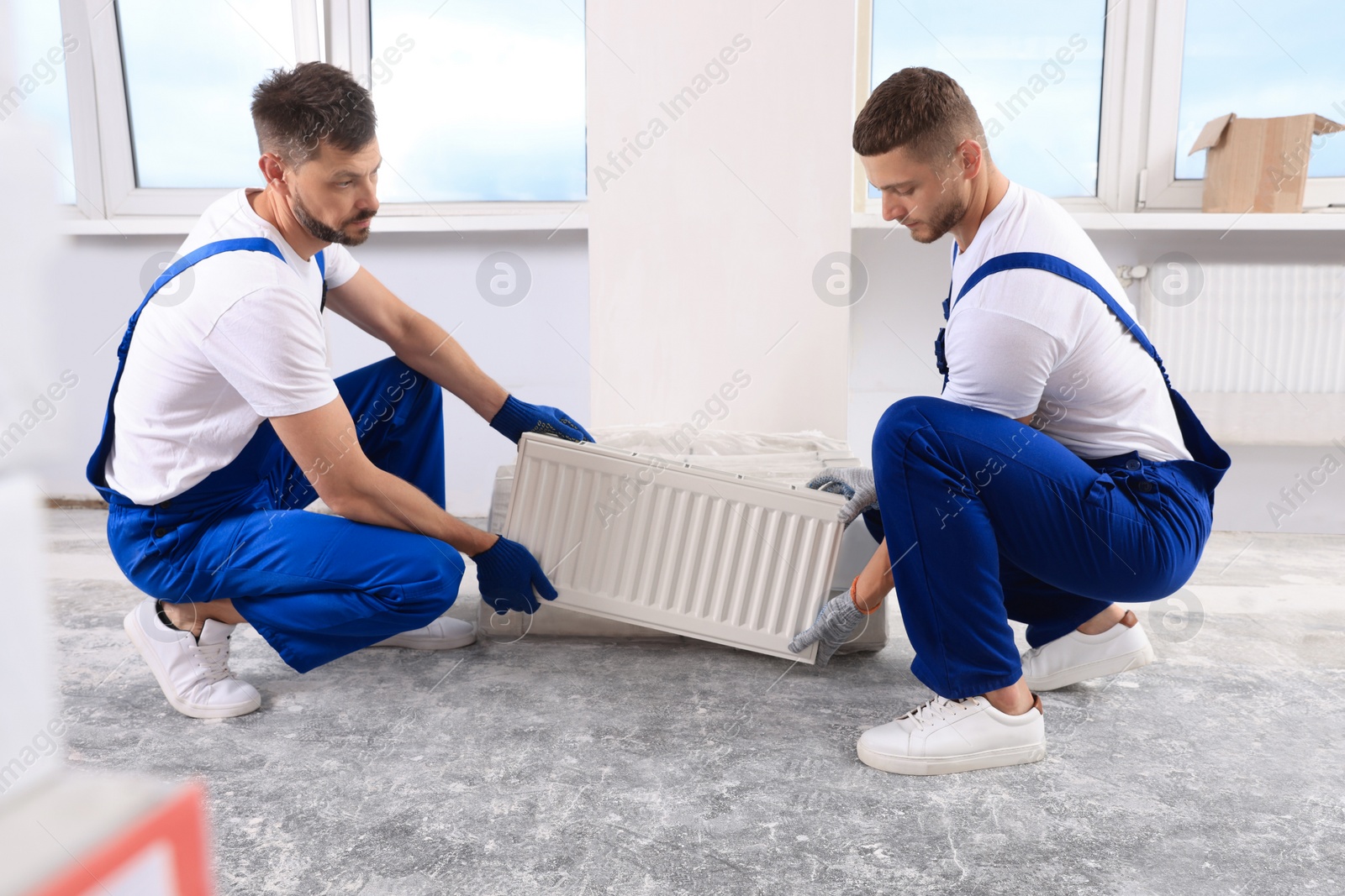 Photo of Professional plumbers with new heating radiator in room