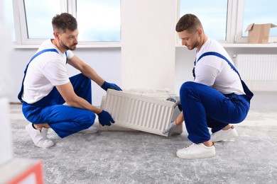 Professional plumbers with new heating radiator in room