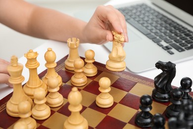 Photo of Woman playing chess with partner through online video chat at white table, closeup