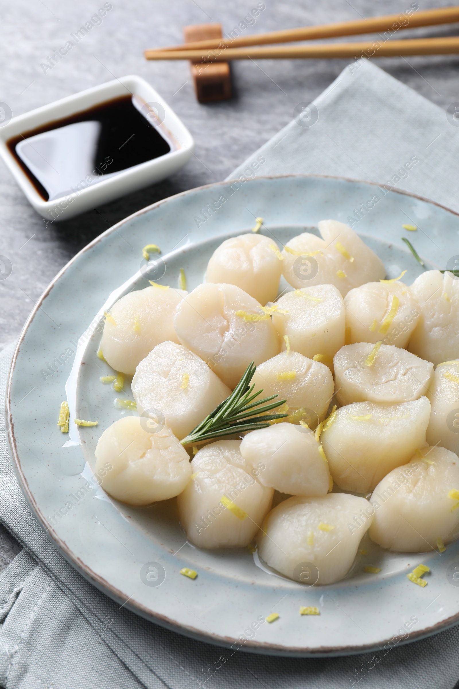 Photo of Raw scallops with lemon zest and rosemary on grey table, closeup