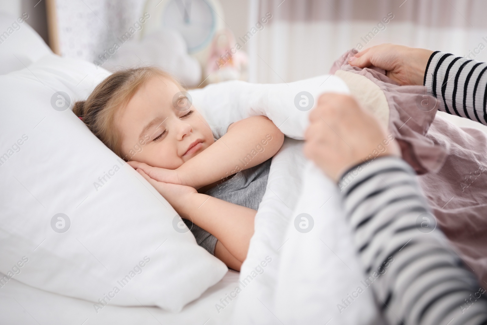 Photo of Mother putting her cute little daughter to sleep at home