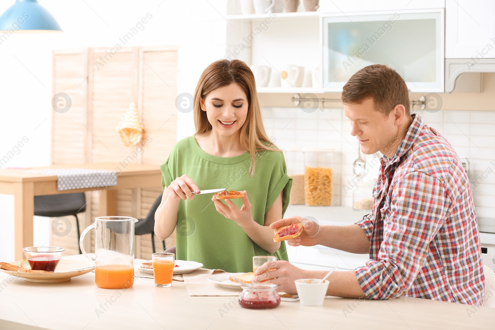 Photo of Happy lovely couple having breakfast with tasty toasted bread at table in kitchen