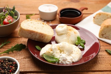 Photo of Delicious burrata cheese with basil on wooden table, closeup