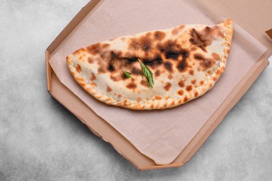 Cardboard box with delicious calzone on grey table, top view