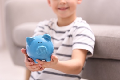 Little boy with piggy bank at home, closeup