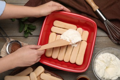 Woman making tiramisu cake at wooden table, top view