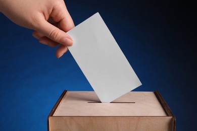 Photo of Woman putting her vote into ballot box on dark blue background, closeup