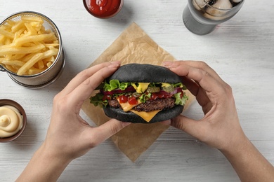 Woman holding black burger at served table, top view