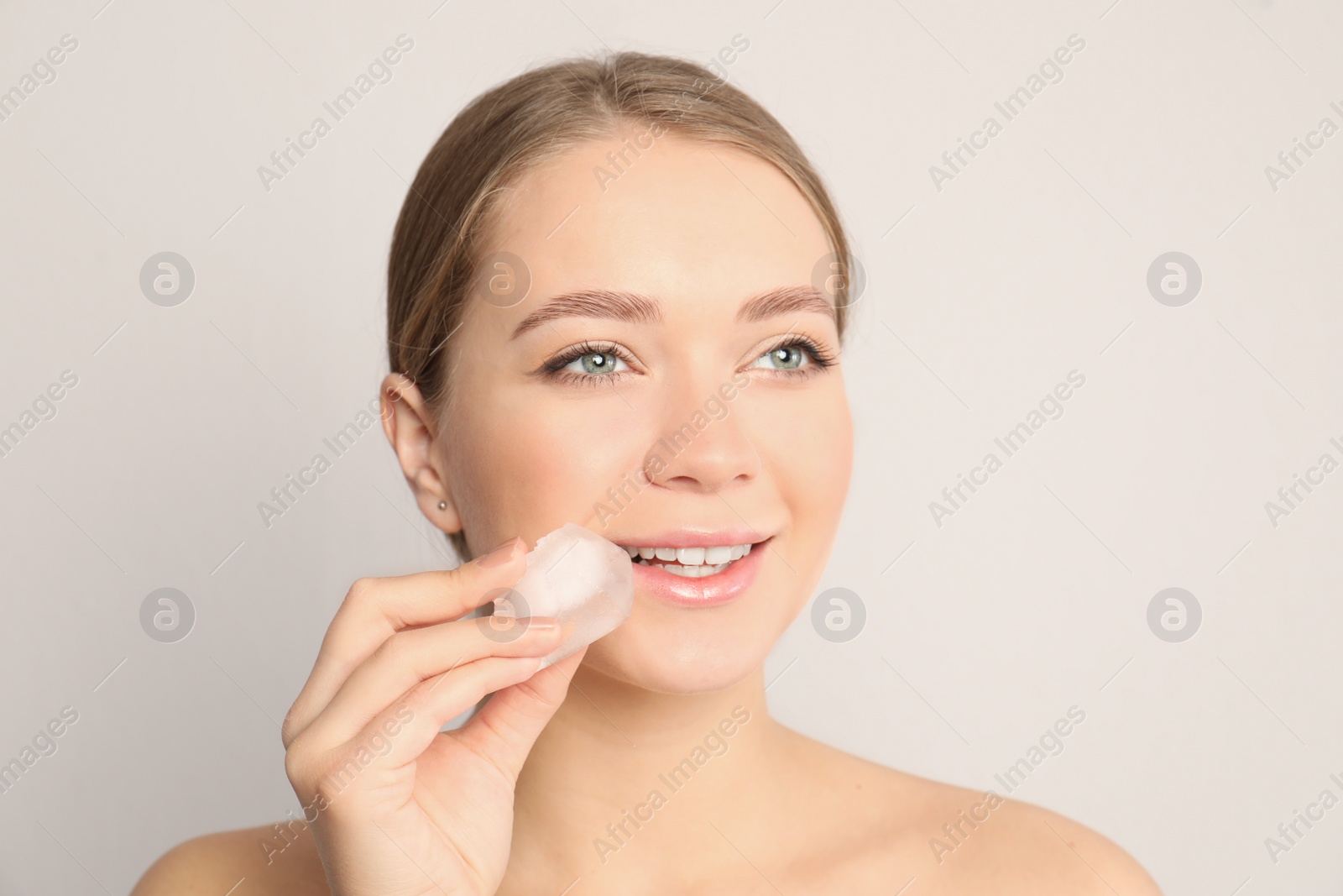 Photo of Young woman with ice cube on light background. Skin care