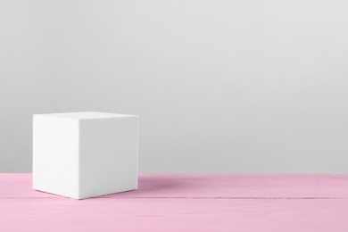 Photo of White cube podium on pink wooden table. Space for text