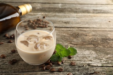 Photo of Coffee cream liqueur in glass, mint and beans on wooden table, space for text
