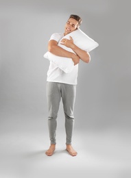 Photo of Young man in pajamas embracing pillow on gray background