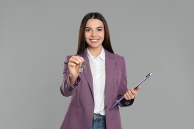 Photo of Female real estate agent with key and clipboard on grey background