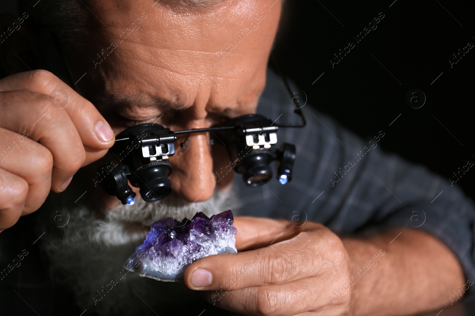 Photo of Male jeweler evaluating amethyst in workshop, closeup view