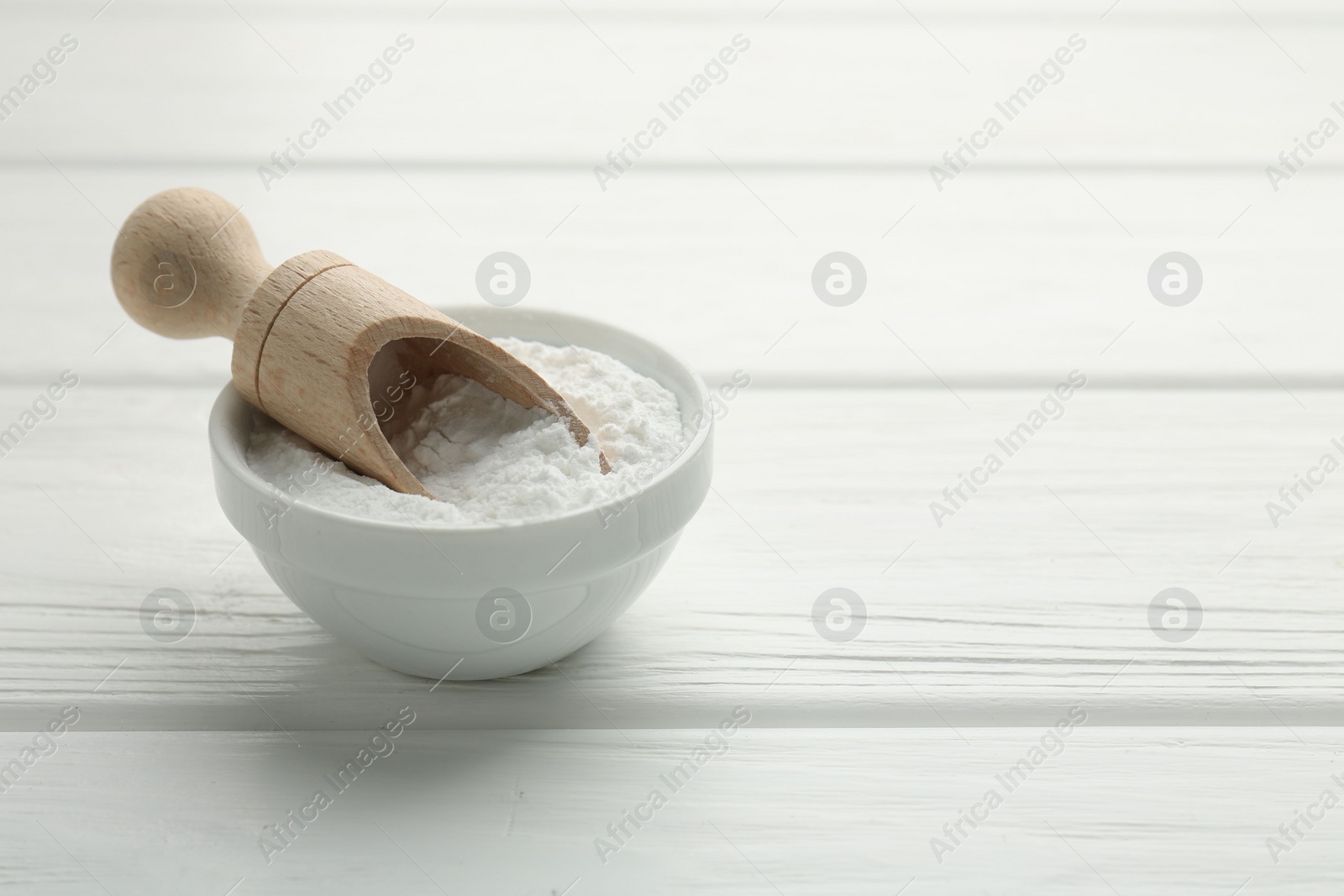 Photo of Baking powder in bowl and scoop on white wooden table, space for text