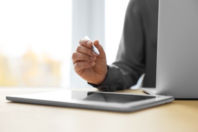 Woman with tablet and pen working on laptop at wooden table, closeup. Electronic document management