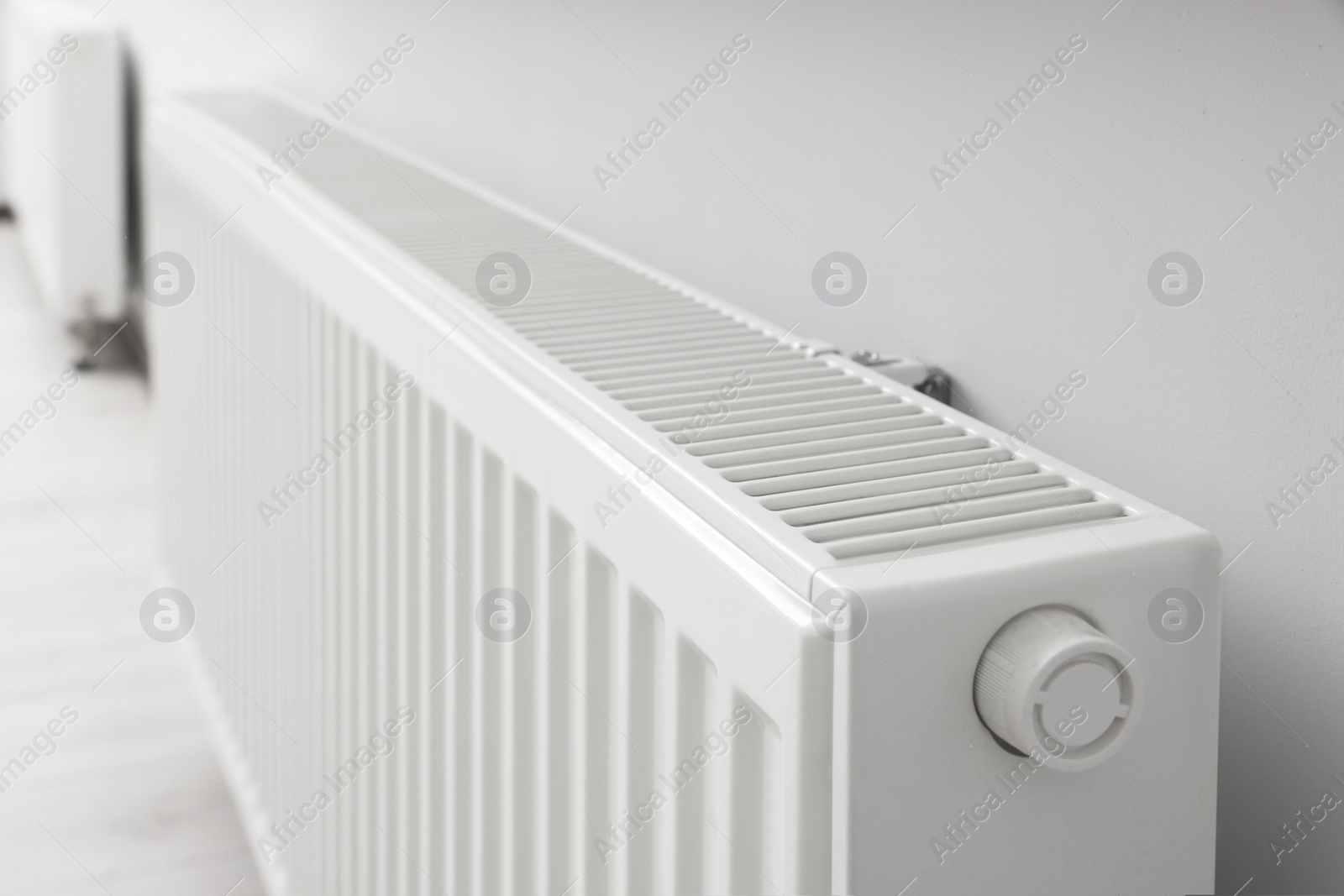 Photo of Modern radiator on white wall in room, closeup. Central heating system