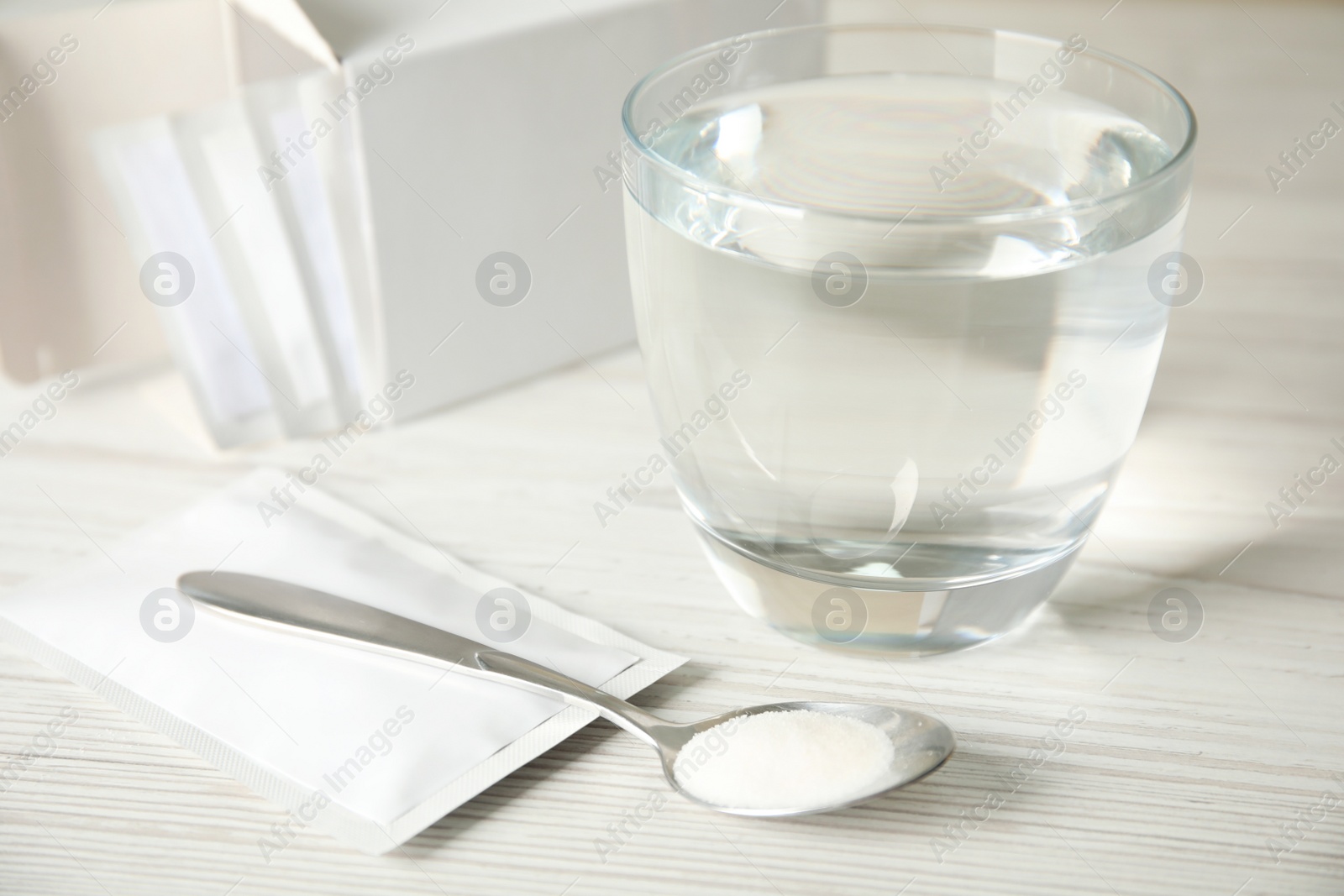 Photo of Medicine sachets, glass of water and spoon on white table