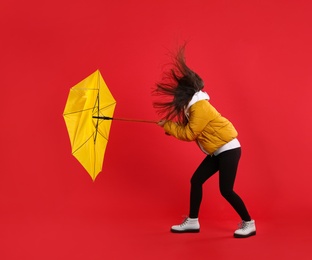 Photo of Woman with umbrella caught in gust of wind on red background