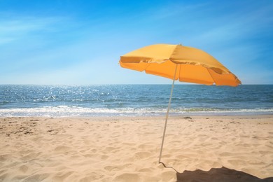 Orange beach umbrella on sandy seashore, space for text