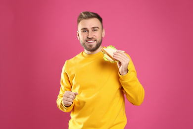 Young man with tasty sandwich on pink background